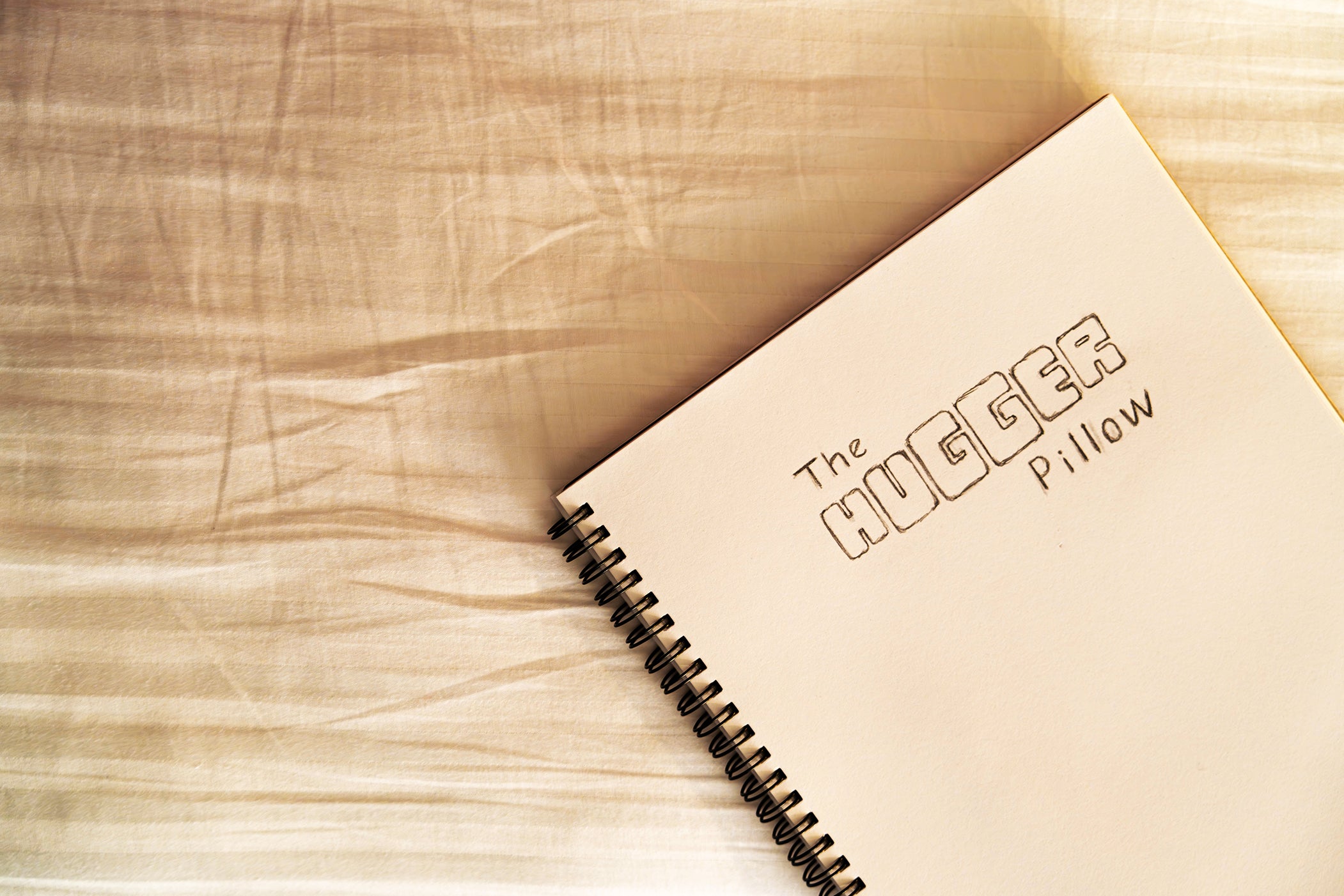 Banner image of a top down view of The Hugger Pillow logo hand drawn on a sketch book - this is an actual image of the logo before it was designed in Adobe Illustrator.